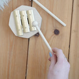 Adult hand holding a wooden mallet over the Auris 3 tone glockspiel on a wooden floor