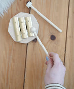 Adult hand holding a wooden mallet over the Auris 3 tone glockspiel on a wooden floor