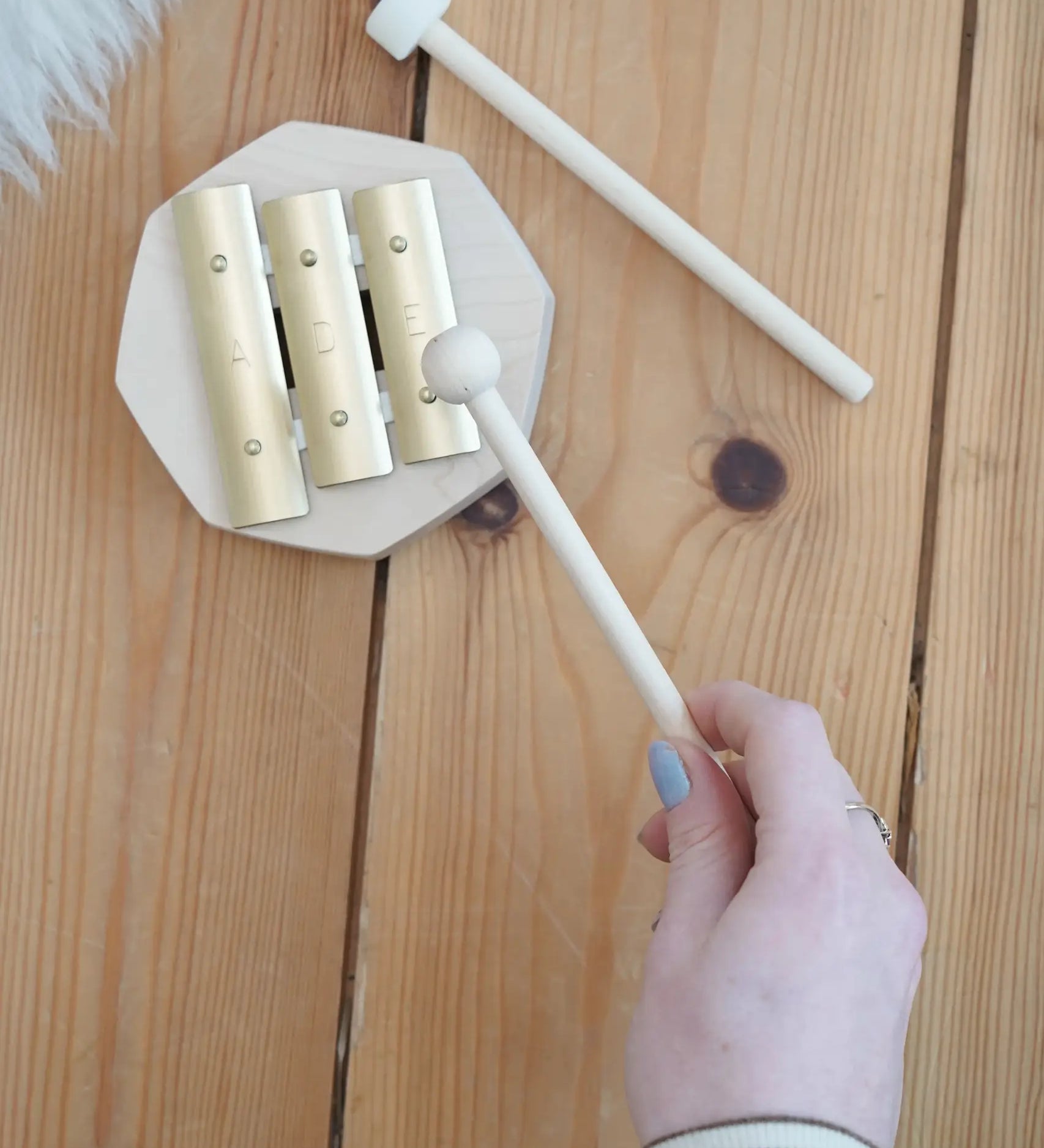 Adult hand holding a wooden mallet over the Auris 3 tone glockspiel on a wooden floor