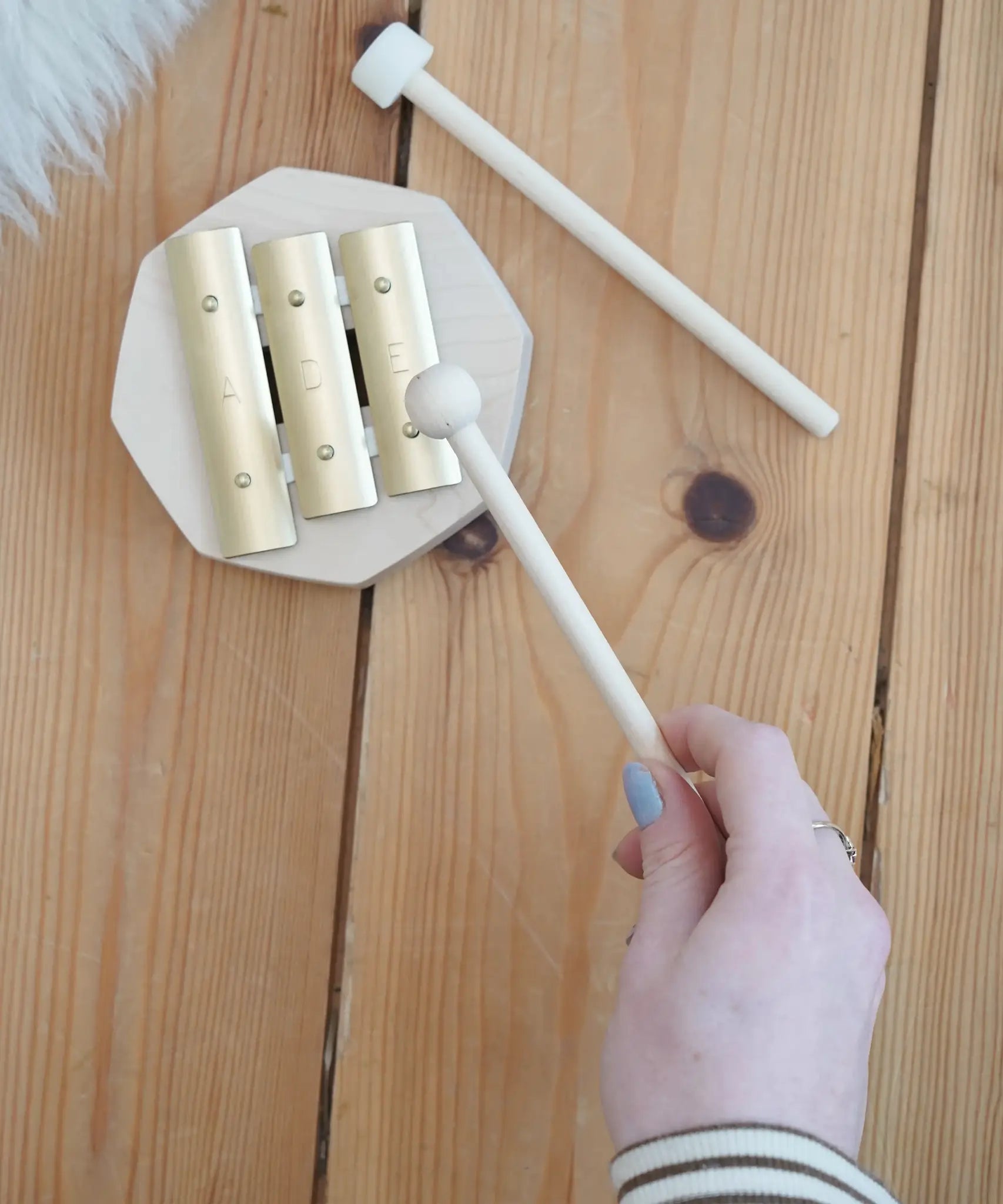 Adult hand holding a wooden mallet over the Auris 3 tone glockspiel on a wooden floor