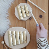 Auris junior 3 tone and junior glockenspiel on a wooden floor with a adult hand holding a wooden mallet