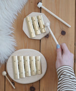 Auris junior 3 tone and junior glockenspiel on a wooden floor with a adult hand holding a wooden mallet
