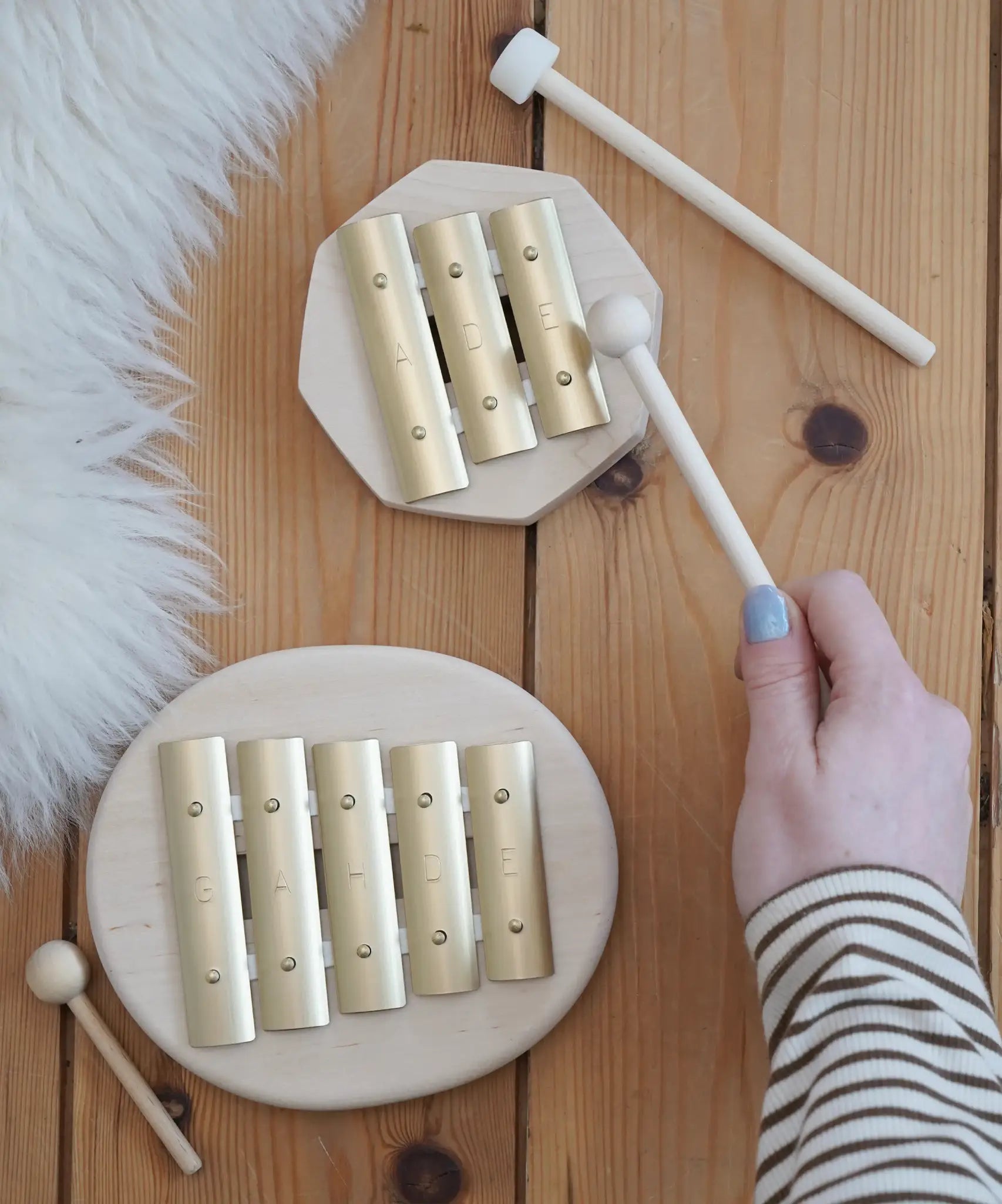 Auris junior 3 tone and junior glockenspiel on a wooden floor with a adult hand holding a wooden mallet