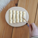 Adult hand holding a wooden mallet over the Auris junior glockspiel on a wooden floor
