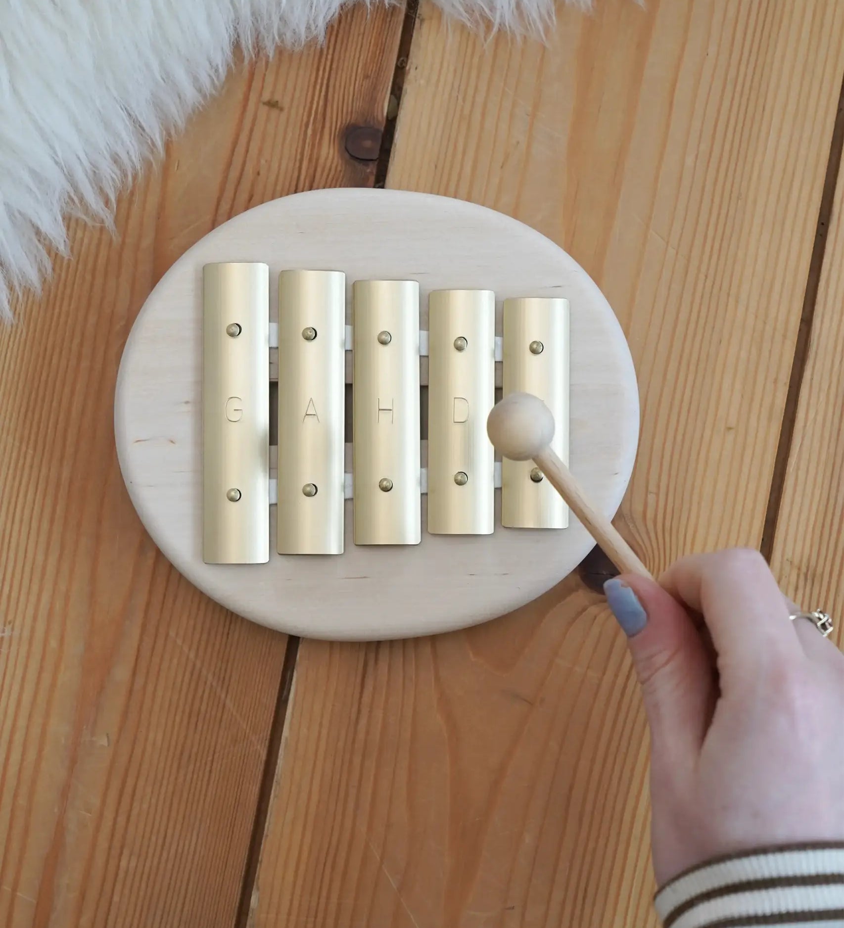 Adult hand holding a wooden mallet over the Auris junior glockspiel on a wooden floor