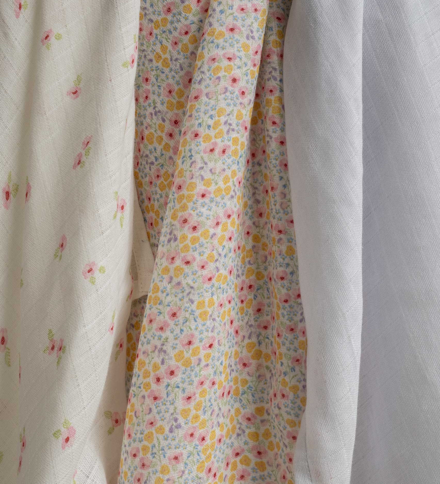 A close up of the design on the cloths from the Avery Row Wildflower Baby Muslin Squares in a Set of 3. One cloth is plain white, one has delicate pink flowers and one has an all over floral wildflower design. Avery Row have a collection of stylish nursery and baby essentials available at Babipur.