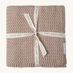 A soft dusty pink plait knitted Avery Row blanket on a cream background.