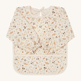 A light cream Avery Row long sleeve  baby bib with a grassland design on a cream background.