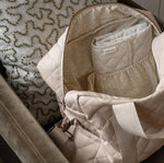 A close up of the Avery Row Baby Changing Bag in a  Natural colour with the zip opened reveling the sateen lining with a delicate floral chamomile print. 