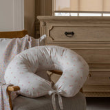 An Avery Row Nursing Pillow with an Anemone design placed on a chair in a nursery. The The top of the pillow features a white background with a delicate pink anemone flower print. Avery Row have a range of baby and nursery products with stylish designs available at Babipur. 