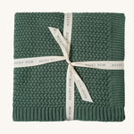 A pine green Avery Row knitted blanket on a cream background