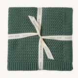 A pine green Avery Row knitted blanket on a cream background