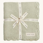 A soft willow colour Avery Row knitted blanket on a cream background.