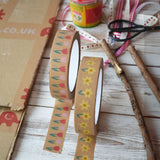 A roll of tulip and a roll of daffodils kraft paper tape from Babipur with a bit rolled out on each and placed on a wooden surface. Craft supplies can be seen in the background. 
