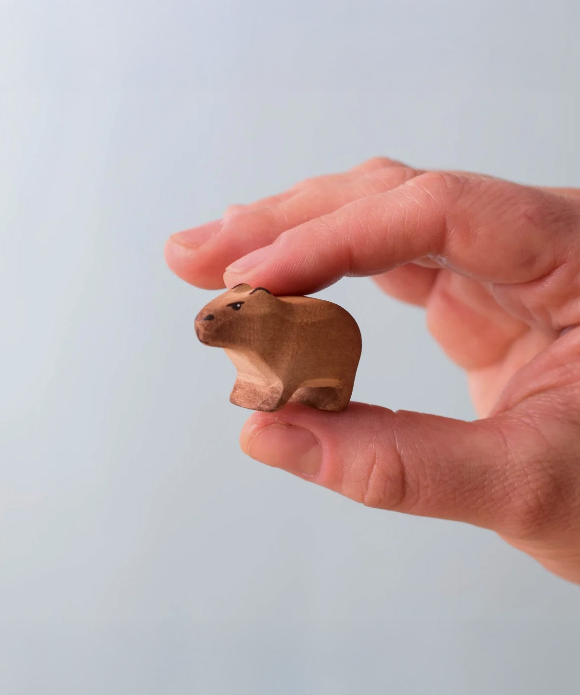 Bumbu Toys Wooden Baby Capybara, being held in an adult's hand.