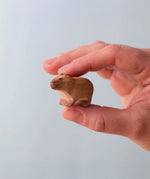 Bumbu Toys Wooden Baby Capybara, being held in an adult's hand.