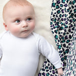 A baby looking up towards the Etta Loves Extra Large Organic Cotton Baby Muslin Square - Purple Leopard next to them. The image shows the vibrancy of the colours