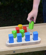 Bajo 10 piece sorting board. Wooden triangle base with 10 slots, 4 square, 3 triangle, 2 rectangle and 1 circle with 10 blocks to fit inside. Child's hand placing a green triangle block onto the base.