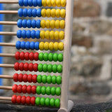 Side of the Bajo 100 Bead Abacus counting toy placed on a stone wall outdoors. 