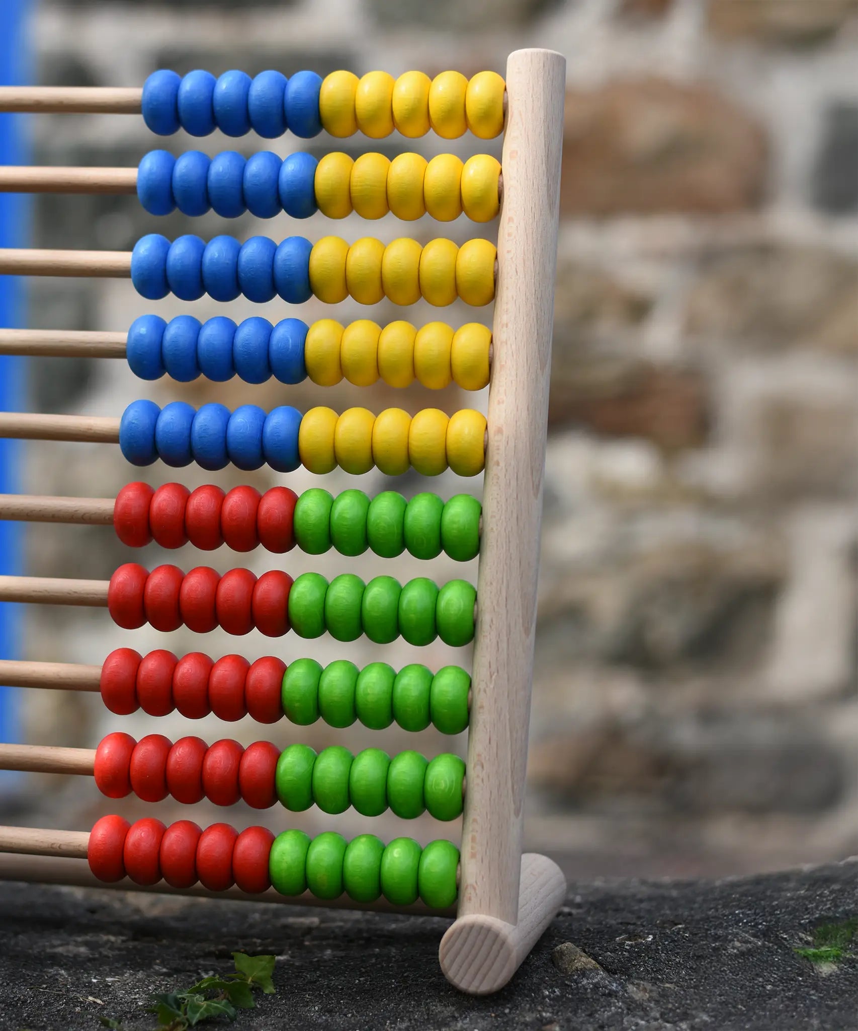 Side of the Bajo 100 Bead Abacus counting toy placed on a stone wall outdoors. 