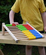 Bajo 100 Bead Abacus counting toy placed on a Miri slide set up as a table outoors.