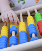 Close up of a child's hand playing with the Bajo 100 Bead Abacus counting toy. 
