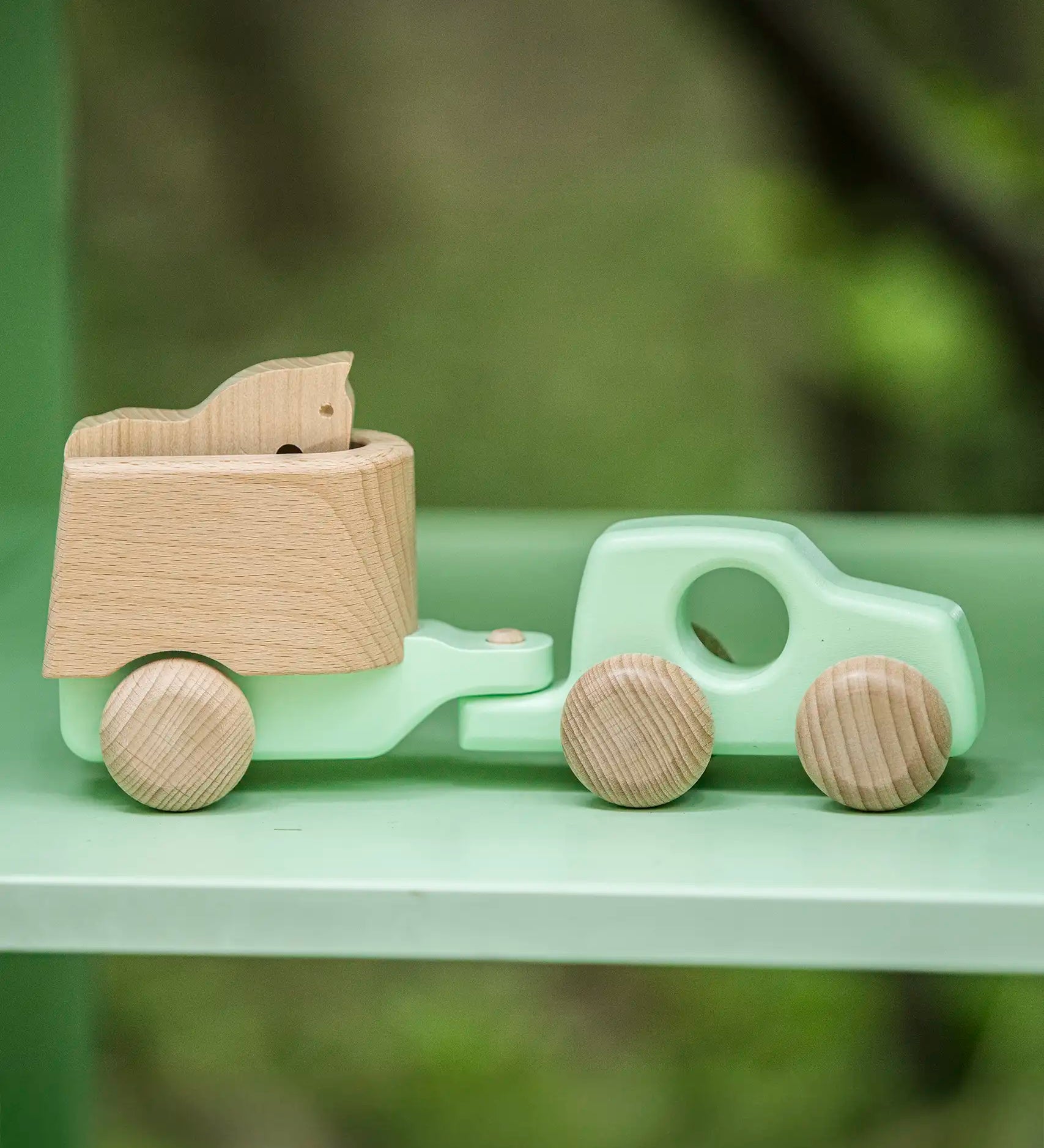 Bajo mint green 4x4 car and horse trailer wooden toy placed on a shelf.