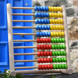 Bajo 100 Bead Abacus counting toy placed on a stone wall outdoors. 