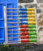 Bajo 100 Bead Abacus counting toy placed on a stone wall outdoors. 