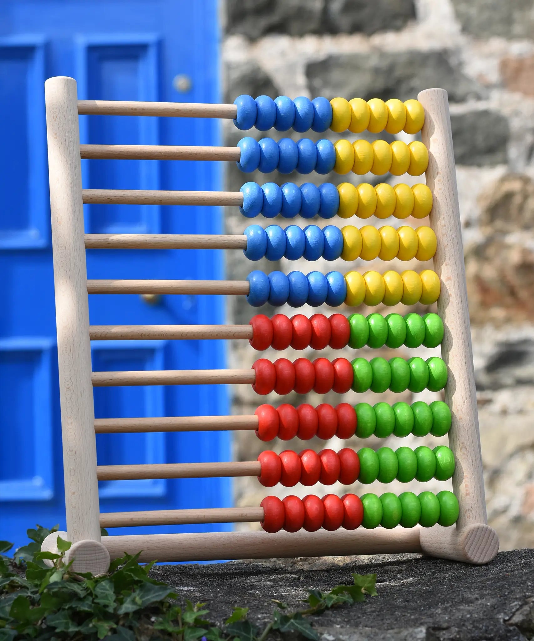 Bajo 100 Bead Abacus counting toy placed on a stone wall outdoors. 