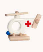 Bajo Ambulance Helicopter wooden toy. A white painted helicopter with a red cross and natural wooden stands and propellors. These heirloom quality toys by Bajo are part of a wide range of wooden toys available here at Babipur. 