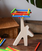 Bajo athlete wooden stacking balance game placed on a wooden surface with some of the wooden sticks balanced on the athlete shaped wooden figure base. 