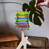 Bajo athlete wooden stacking balance game with wooden sticks balanced on the athlete shaped wooden figure base. An adult's hand can be seen placing another stick on the stack  