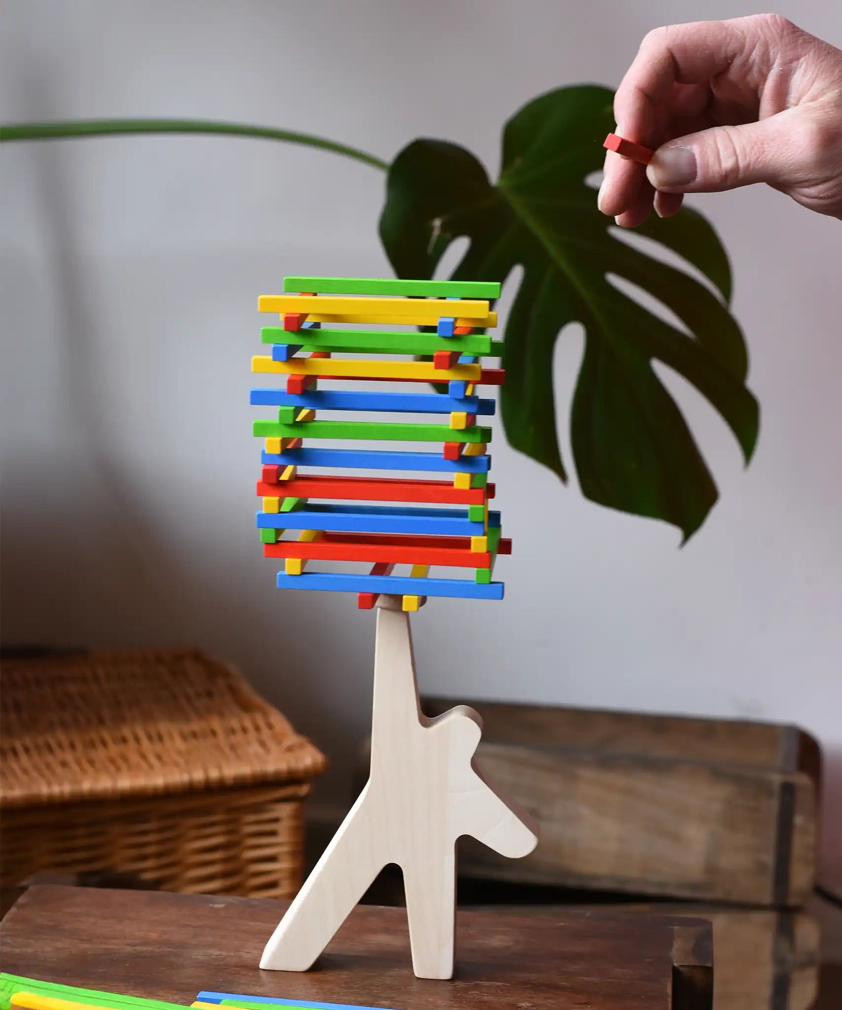 Bajo athlete wooden stacking balance game with wooden sticks balanced on the athlete shaped wooden figure base. An adult's hand can be seen placing another stick on the stack  