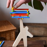 Bajo athlete wooden stacking balance game with wooden sticks balanced on the athlete shaped wooden figure base. An adult's hand can be seen placing another stick on the stack  