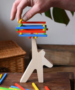 Bajo athlete wooden stacking balance game with wooden sticks balanced on the athlete shaped wooden figure base. An adult's hand can be seen placing another stick on the stack  