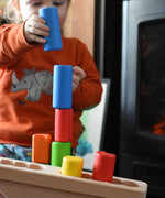 A child stacking the blocks from the Bajo Balance Scale wooden toy on top of each other. A wooden base with a curved base with coloured wooden blocks that sit on top. These heirloom quality toys by Bajo are part of a wide range of wooden toys available here at Babipur.