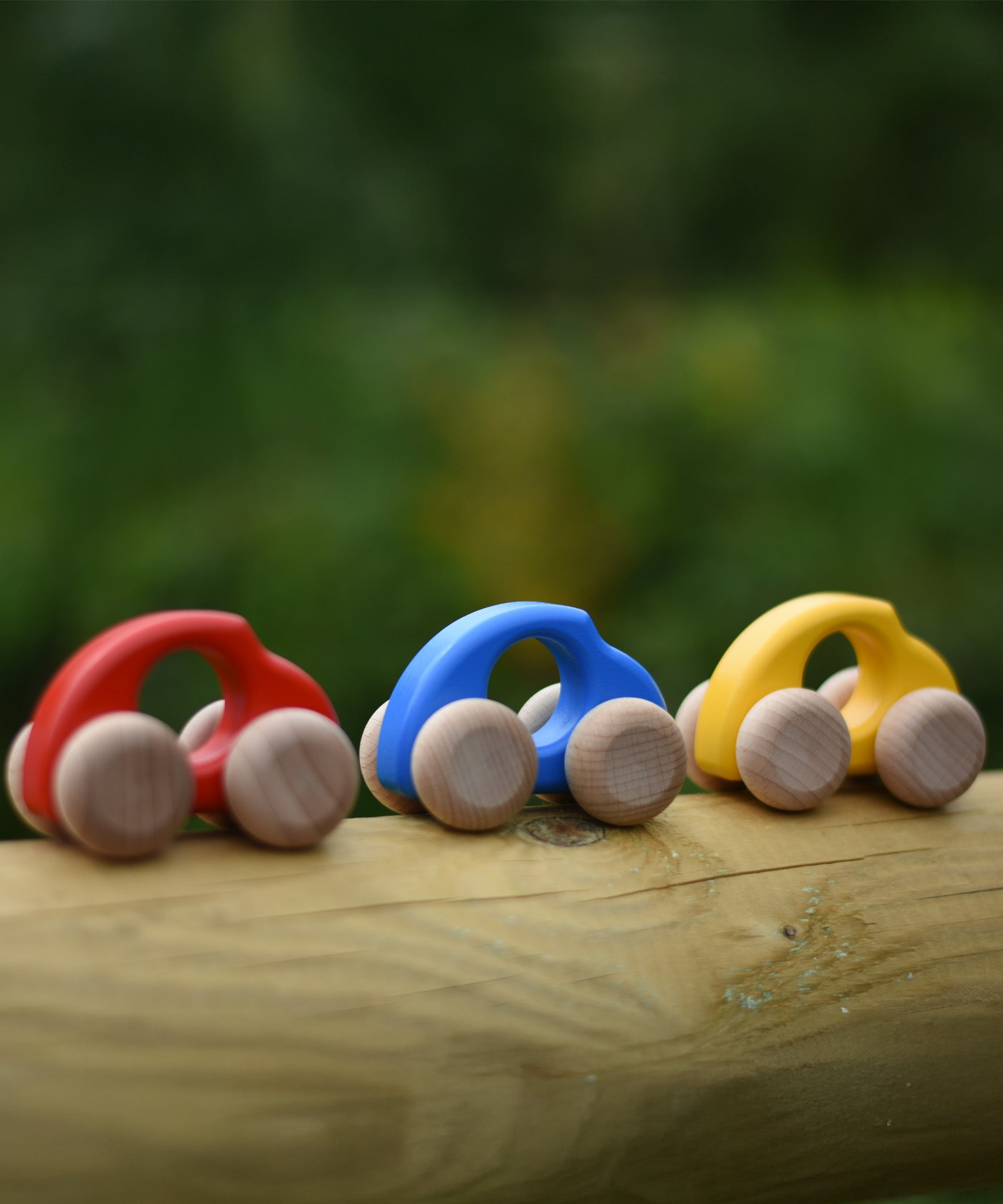 A group of Bajo handmade wooden beetle style car including blue, yellow and red available at Babipur - photo on a outdoor background.