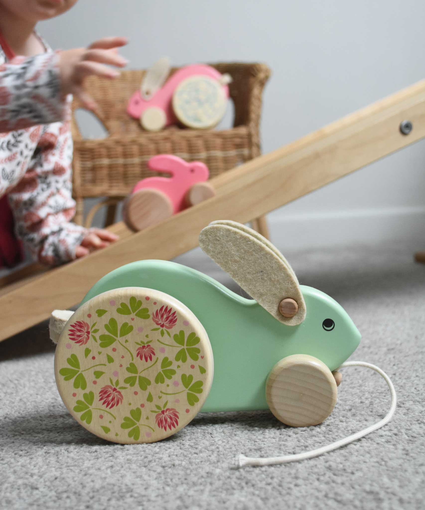 The mint Bajo big rabbit placed on the floor in front of a Triclimb Miri slide. A child can be seen in the background placing a pink coloured small push along rabbit on the Miri slide. These heirloom quality toys by Bajo are part of a wide range of wooden toys available here at Babipur.