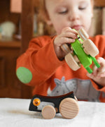 A Bajo Pull-Back black Caterpillar Toy placed on a table in front of a child. A black coloured caterpillar toy that has a yellow eye and natural wooden wheels.  These heirloom quality toys by Bajo are part of a wide range of wooden toys available here at Babipur.