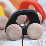 A Bajo handmade wooden black mini car available at Babipur. Features unpainted wheels and a cut out hole for a easy hold. Photo is in a playroom setting