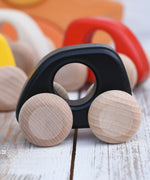 A Bajo handmade wooden black mini car available at Babipur. Features unpainted wheels and a cut out hole for a easy hold. Photo is in a playroom setting