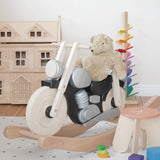 Bajo wooden black rocking bike with a senger teddy bear on top showing scale with a doll house and marble tree in the background