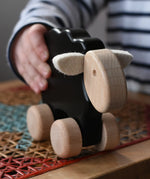 Child playing with the Bajo black sheep push along wooden toy on wheels in the Babipur playroom.