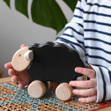 Child reaching for the Bajo black sheep push along wooden toy on wheels placed a rattan stool in the Babipur playroom.