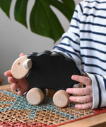 Child reaching for the Bajo black sheep push along wooden toy on wheels placed a rattan stool in the Babipur playroom.