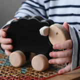 Child holding for the Bajo black sheep push along wooden toy on wheels placed a rattan stool in the Babipur playroom.