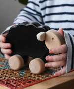 Child holding for the Bajo black sheep push along wooden toy on wheels placed a rattan stool in the Babipur playroom.