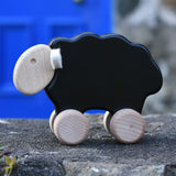 Bajo black sheep push along wooden toy on wheels placed on a stone wall outdoors.