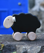 Bajo black sheep push along wooden toy on wheels placed on a stone wall outdoors.